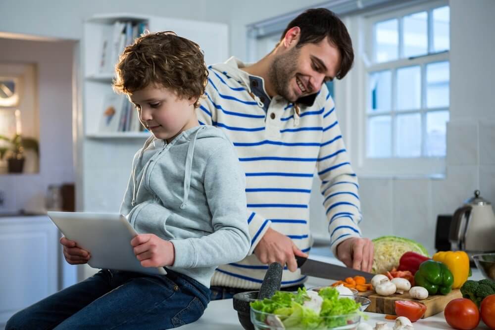 Father talking on mobile phone while chopping vegetables and son using digital tablet in the kitchen.jpeg